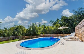 Relax by the oval-shaped pool surrounded by lush greenery and a tiled deck.