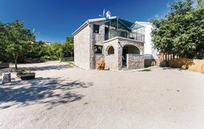 Standalone building with a modern design, featuring a balcony with a glass enclosure, surrounded by lush greenery and a gravel driveway.
