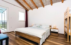 Cozy retreat with a large bed, bedside table, and wooden bunk bed, offering a view of the outdoors.