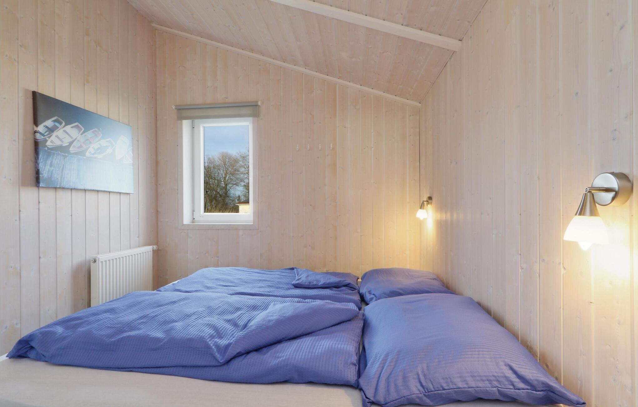 Een slaapkamer met een houten plafond, een raam, een radiator en twee bedlampen.