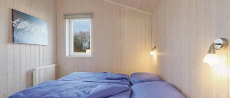 Een slaapkamer met een houten plafond, een raam, een radiator en twee bedlampen.