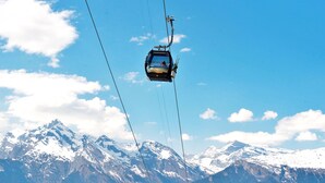 A cable car ascending a mountain with a clear sky and snow-covered peaks in the background.