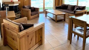 A spacious living area with wooden furniture, a fireplace, and large windows offering a view of the outdoors.