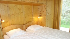 A wooden room with a bed, a nightstand, and a wall-mounted light.