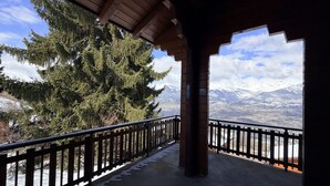 Un balcone coperto con vista su montagne innevate e un grande abete sempreverde.