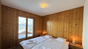 Una stanza con rivestimenti in legno, un letto, due comodini e una finestra con vista sulle montagne.