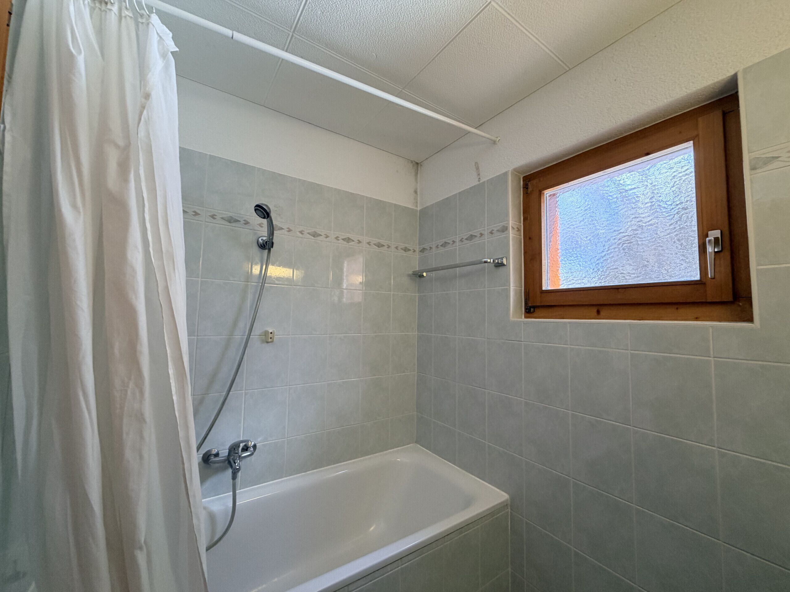 A bathroom with a bathtub, shower, and a window with frosted glass.