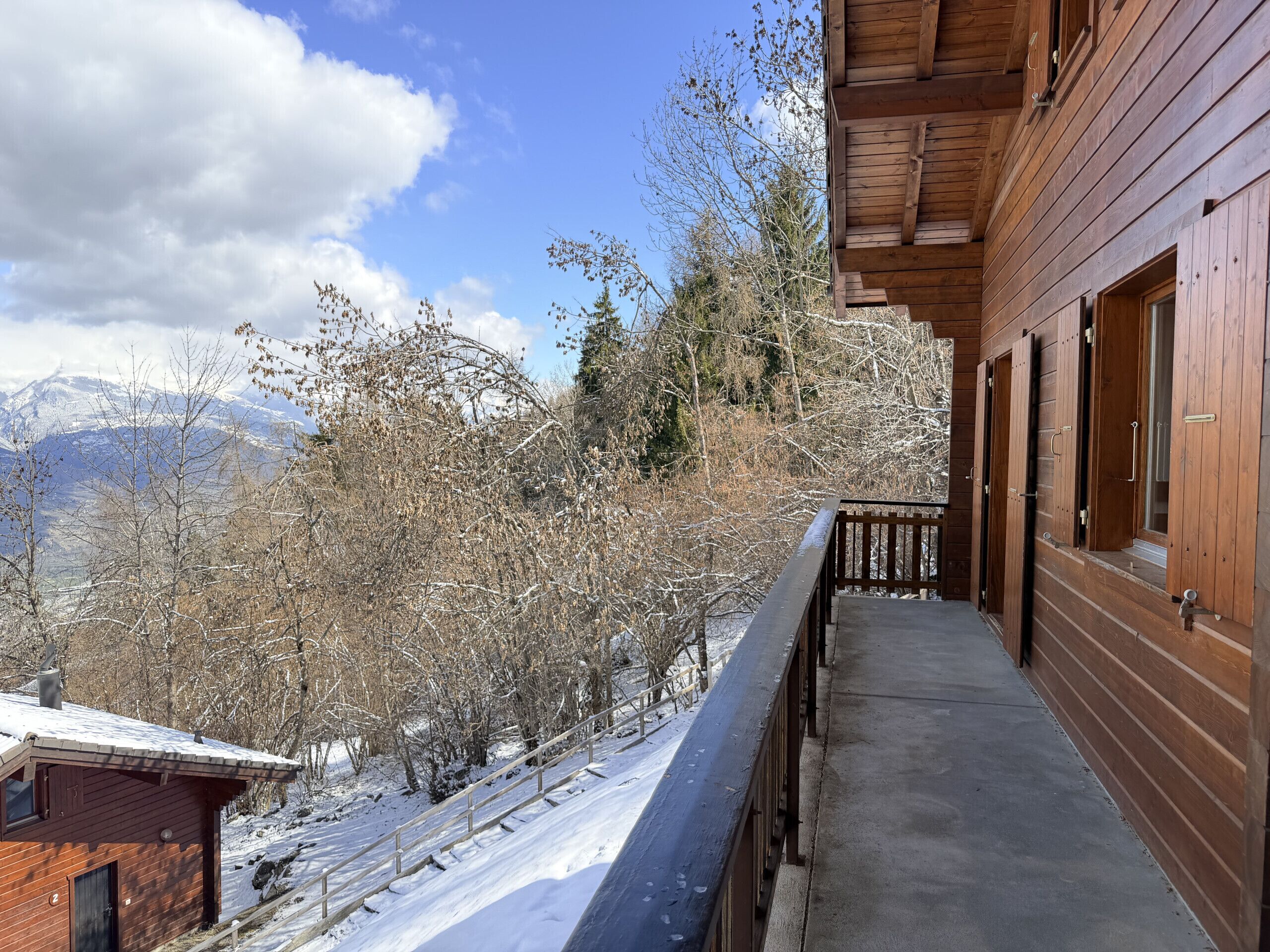 Eine Holzhütte mit einem Balkon mit Blick auf eine verschneite Landschaft und Berge.