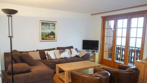 A living room with a brown sectional sofa, a coffee table, and leather armchairs. A flat-screen TV is on a stand, and there's a painting on the wall. - HCR 141 - COMFORTABLE apartment 8 pers (Veysonnaz)