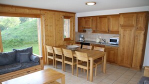 Un intérieur en bois comprenant une table à manger, des chaises, un canapé et un coin cuisine avec des meubles et des appareils électroménagers en bois.