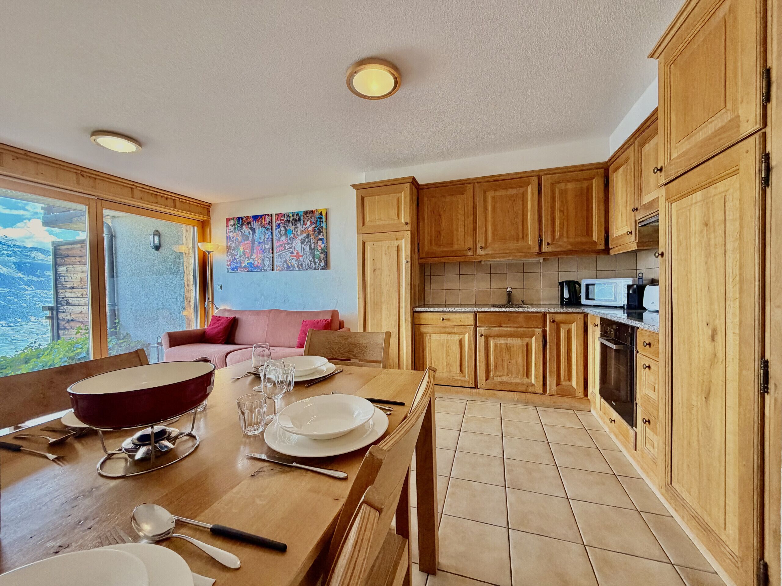 Una cocina moderna con armarios de madera, una mesa de comedor preparada para cuatro comensales y un ventanal con vistas al exterior.
