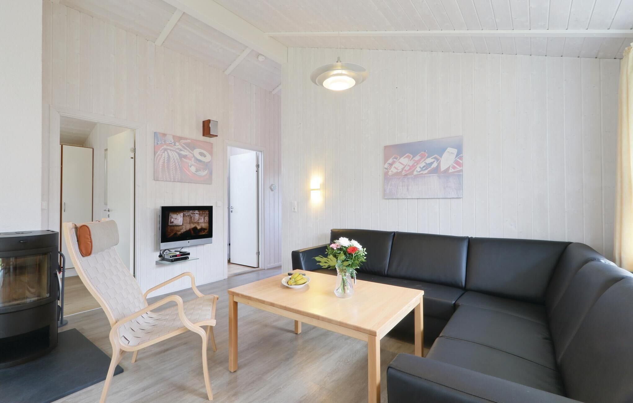 Ett vardagsrum med en svart lädersoffa, ett soffbord i trä, en tv som är monterad på väggen och en öppen spis.