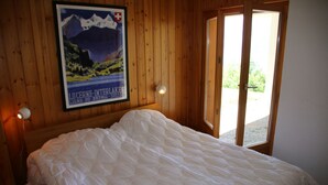 A bedroom with a large bed, wooden walls, a poster, and a door leading to an outdoor area. - Fontannets 006 QUIET & SUPERIOR chalet 10 pers (Salins)