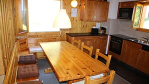 A wooden interior with a dining table, benches, and a kitchen area including a stove and sink. - Fontannets 006 QUIET & SUPERIOR chalet 10 pers (Salins)