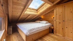 A wooden room with a skylight, a bed, a wardrobe, and a small stool.