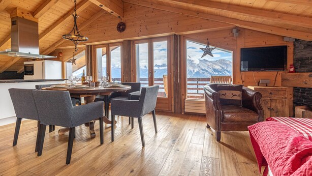 A wooden interior with a dining area, a fireplace, and a large window overlooking mountains.