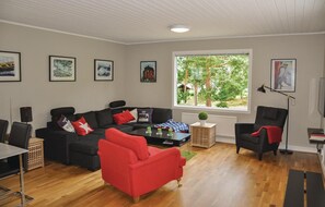 Un salon avec un canapé noir, un fauteuil rouge, une table basse et des tableaux encadrés accrochés au mur.