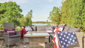Ein Außenbereich mit Korbmöbeln und Kissen mit amerikanischem Flaggenmuster, mit Blick auf einen See.