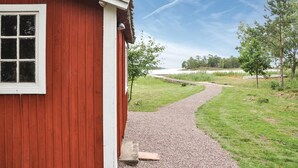 Ein rotes Holzgebäude mit einem Kiesweg, der zu einer Rasenfläche und Bäumen führt.