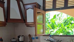 A kitchen with wooden cabinets, a tiled floor, and a window with a view of greenery. - Country house in Guadeloupe (Capesterre Belle Eau)