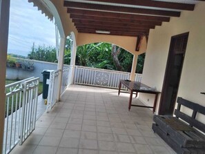 A covered outdoor area with a tiled floor, a wooden bench, and a metal railing.