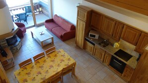 A compact living space with a dining area, a sofa, a kitchen with wooden cabinets, and a sliding glass door leading to an outdoor area.