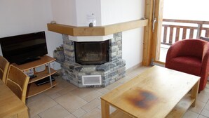 A living room with a stone fireplace, a television on a wooden stand, a red chair, and a wooden table.