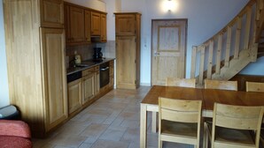 A kitchen with wooden cabinets, a dining table with chairs, and a staircase.