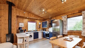 A wooden interior with a kitchen, dining area, and a large window. - Beautiful 5 star, 2 bedroom, 2 bathroom chalet with stunning views and wood burning stove (Crianlarich)
