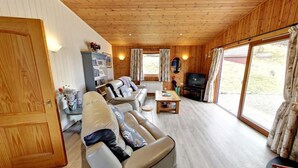 A cozy cabin interior with a sofa, a coffee table, a television, and a bookshelf. - Beautiful 5 star, 2 bedroom, 2 bathroom chalet with stunning views and wood burning stove (Crianlarich)
