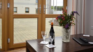Ein Zimmer mit Holztisch, Blumen in einer Vase, einer Flasche, zwei Gläsern und einer Fernbedienung.