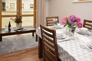 A dining area with a table set for four, a vase with flowers, and a view of the street through large windows. - Apartment 704 Letterfrack - sleeps 5 guests  in 3 bedrooms (Unknown)