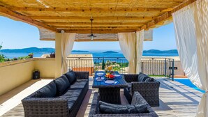 A covered outdoor seating area with wicker furniture, a table set for dining, and a view of the sea. - Cozy home in Brsecine (Brsecine)