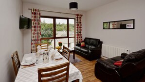 A dining area with a table set for four, a black leather sofa, and a large window with curtains. - Apartment 706 Letterfrack - sleeps 4 guests  in 3 bedrooms (Unknown)