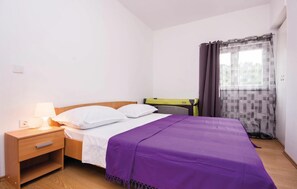 Ein ordentlich eingerichtetes Schlafzimmer mit Bett, Nachttisch, Lampe und einem Fenster mit Vorhängen.