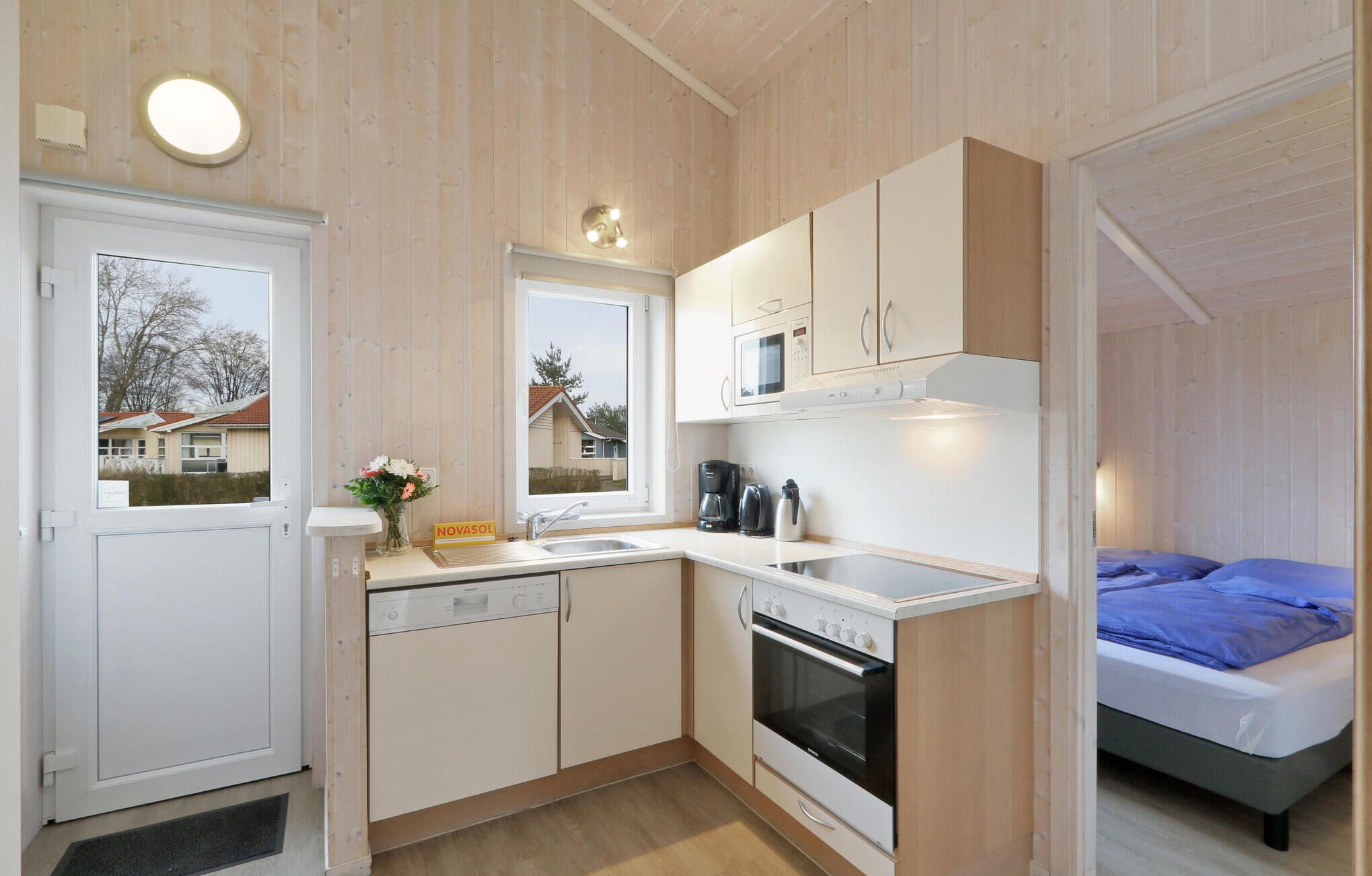 Een compacte keuken met een vaatwasser, oven en magnetron. Een raam biedt uitzicht op huizen.