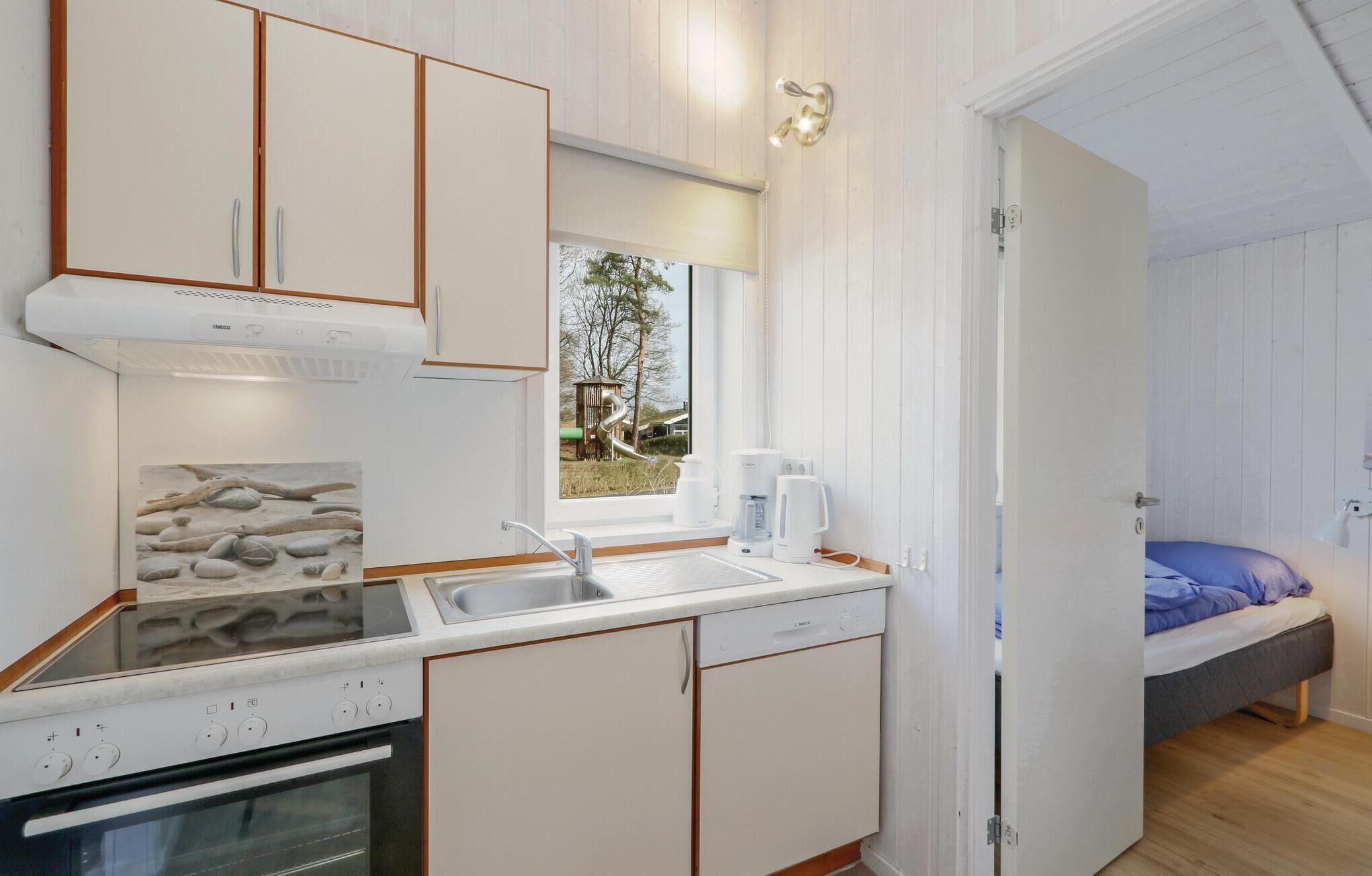 Una cocina compacta con horno integrado, un lavamanos y una ventana con vistas a un parque infantil.