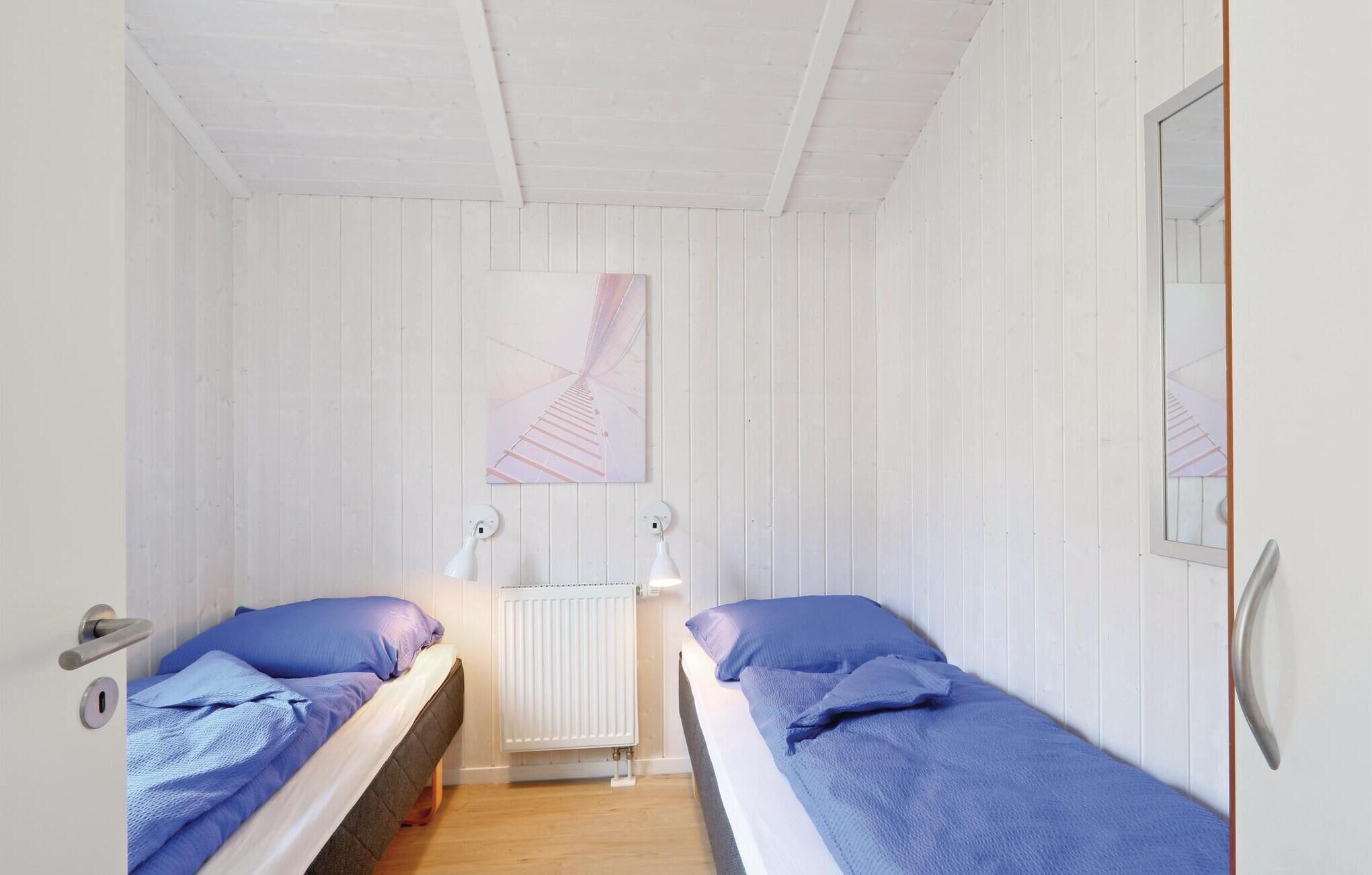A small, narrow room with two single beds, white wooden walls, a white radiator, and a ceiling with exposed beams.