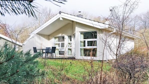 Une maison blanche d’un seul étage, dotée d’un porche abrité, de grandes fenêtres et d’une cheminée.
