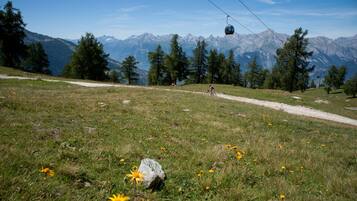 Un paysage de montagne avec un télésiège, un ciel dégagé et un sentier où l’on aperçoit un cycliste.