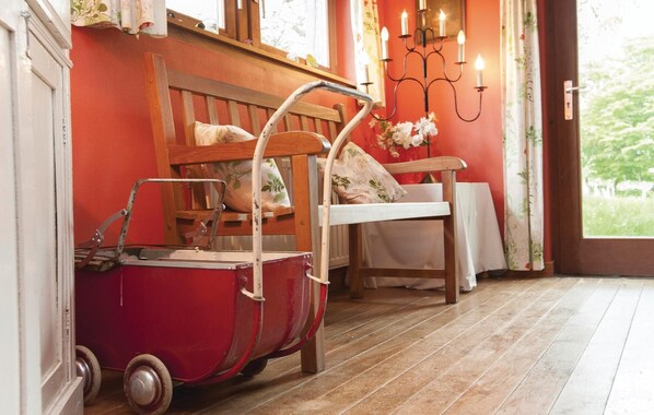 A room with a red wall, a wooden bench, a white chair, a small red cart, and a candelabra with candles. - La Maison d'Albertine (Erezee)