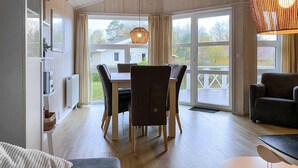 A dining area with a table and chairs, large windows, and a hanging light fixture. - Frische Brise 12 - Dorf 3 (Travemünde-Priwall)