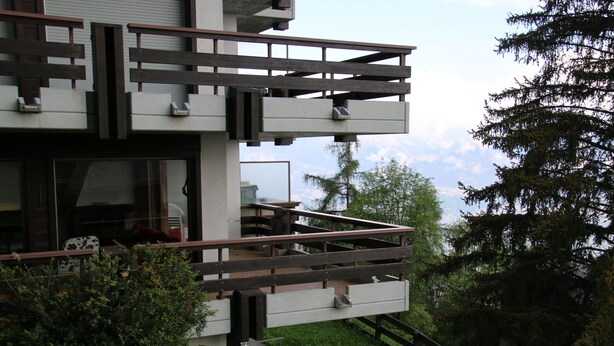 Un bâtiment moderne à deux étages, doté d’un balcon et entouré de verdure et d’arbres.
