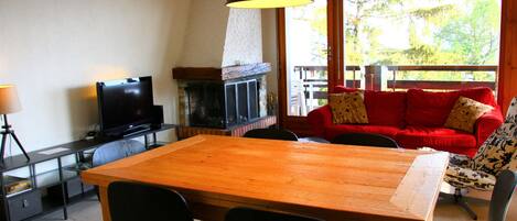 A cozy living room with a wooden table, black chairs, a red sofa, and a fireplace.