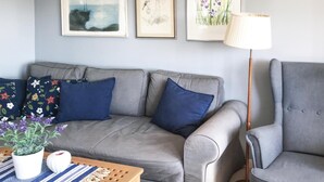 Un divano grigio con cuscini blu, una lampada bianca e quadri appesi al muro.