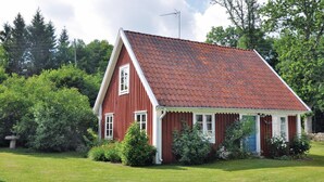 Une maison en bois rouge, avec un toit en pente, entourée de verdure et d’arbres.
