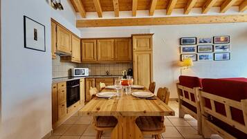 A wooden dining table with chairs, a kitchen with wooden cabinets, a microwave, and a red sofa.