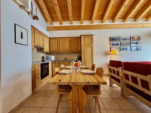 Una mesa de comedor de madera con sillas, una cocina con armarios de madera, un microondas y un sofá rojo.
