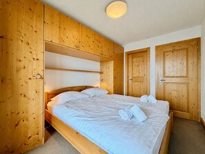 Ein Zimmer mit Holzboden, einem Bett, einer Tür und einer Lampe.