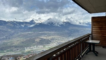 A balcony with a view of snow-capped mountains, a town below, and a wooden railing.